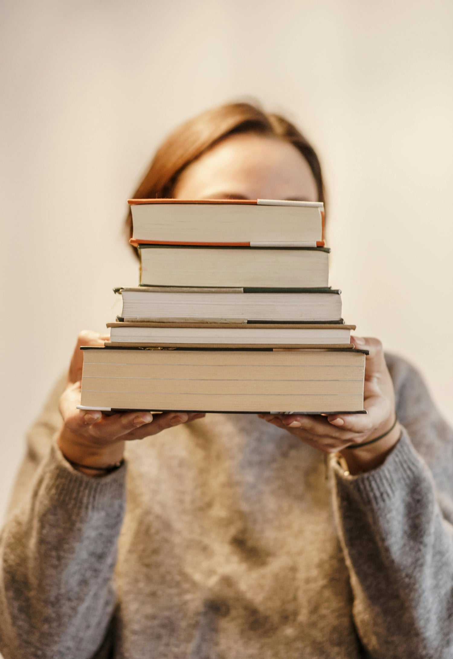 Person holding a stack of books in front of their face, symbolising personalised book recommendations from The Book Muse.